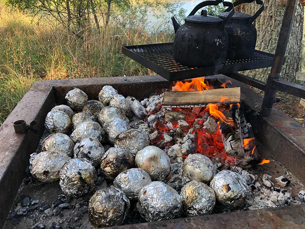 Bakad potatis inrullad i folie och en kaffepanna över grillkol